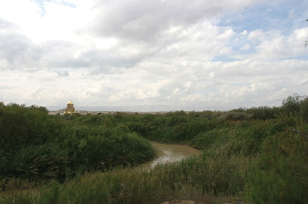 Iordanul şerpuind şi vegetaţia de pe malurile lui. În depărtare, noua Biserică a Sfântului Ioan Botezătorul, construită în ultimii ani